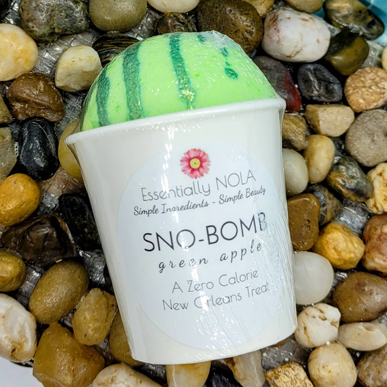 Bath bomb in white cup with green striped top, on tan and white bath rocks