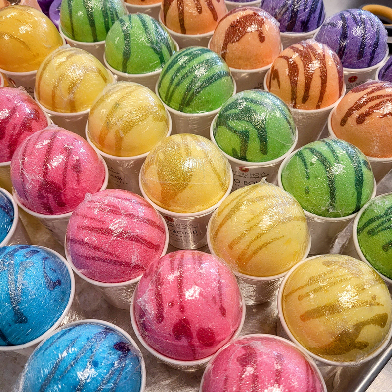 Assorted bath bombs in small cups, glittery pink, blue, green, and orange striped tops
