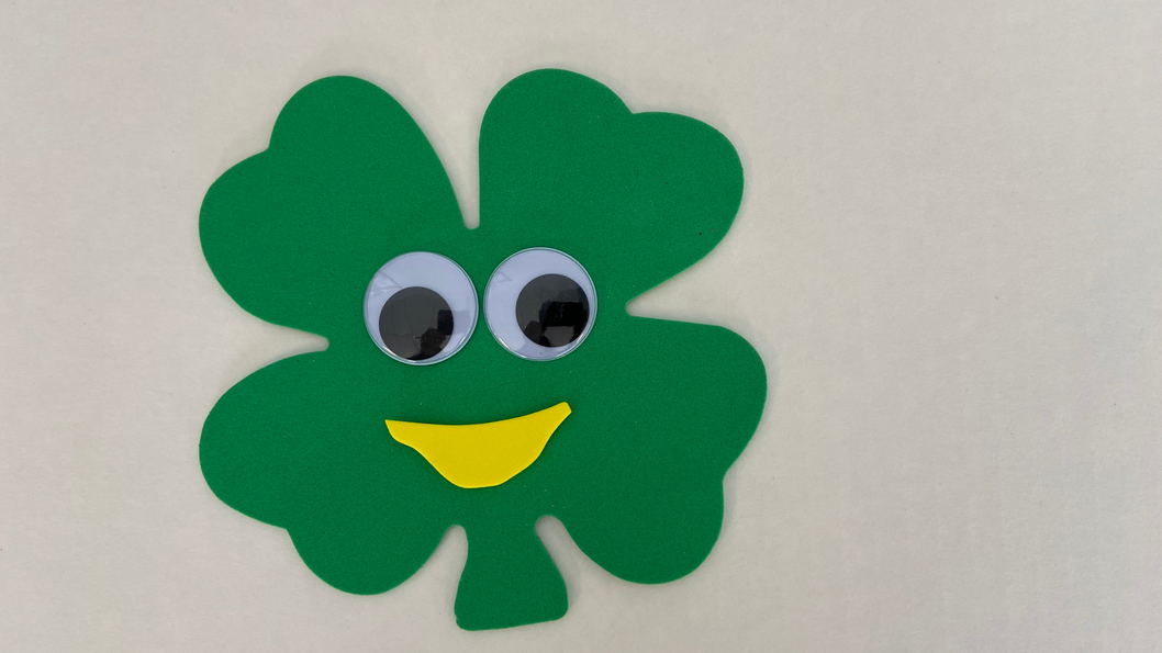 Green foam shamrock cut-out with googly eyes and a yellow smiling mouth