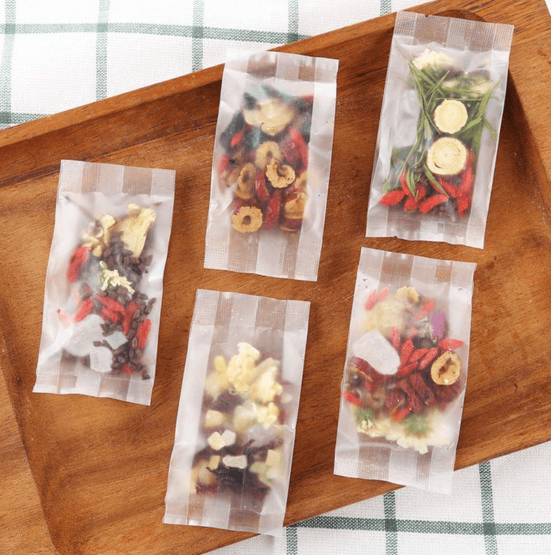 Loose tea sachets with assorted dried flowers and fruit on a wooden tray