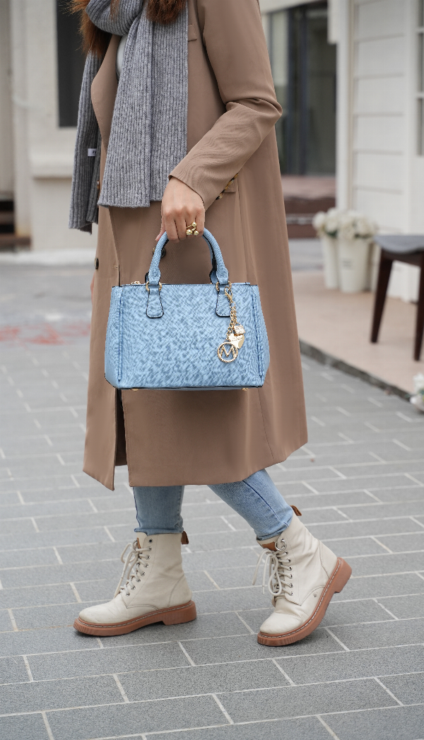 Light blue satchel bag with two top handles and chain charm, carried at side