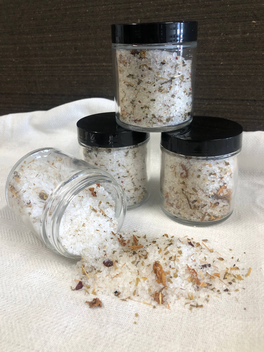 Botanical tea salt soak in glass jars with black lids, spilled granules on cloth