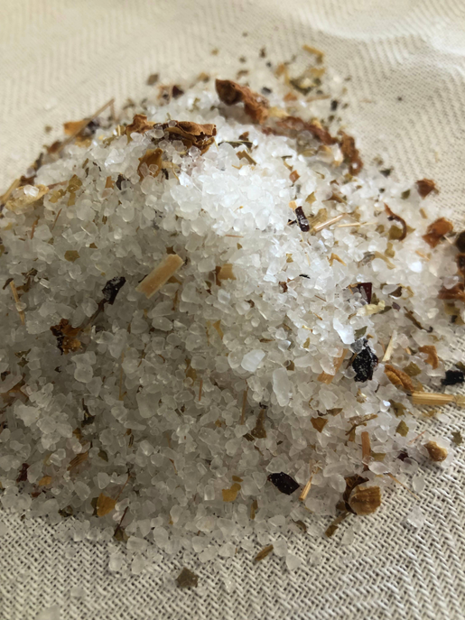 Heap of botanical tea salt soak granules with dried herbs on white fabric
