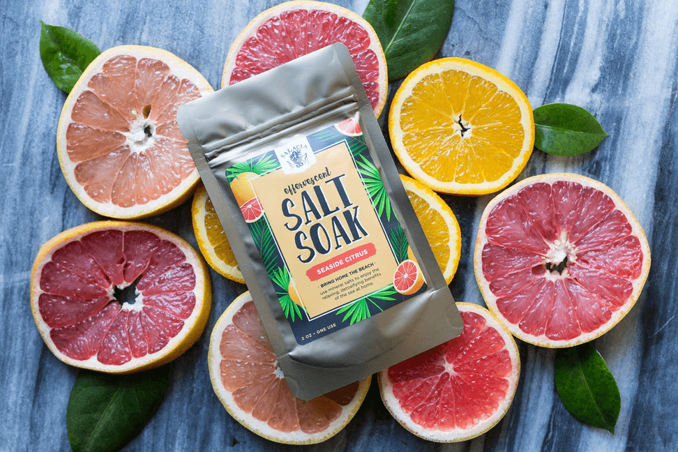 Seaside citrus effervescent salt soak pouch surrounded by citrus slices and leaves.
