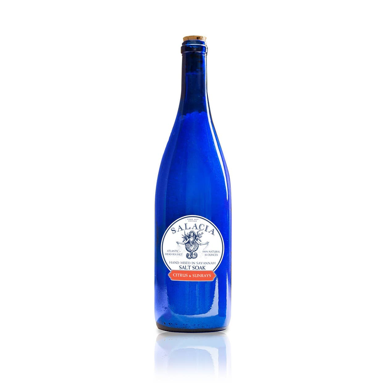 Blue glass salt soak bottle with cork and cream 'SALACIA' label on white
