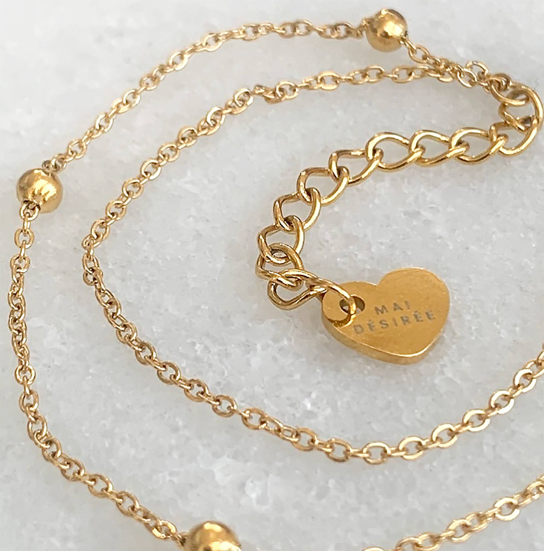 Gold-tone double chain bracelet close-up with heart charm and clasp