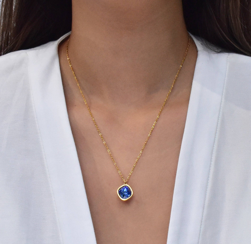Gold chain pendant necklace with round blue sapphire-style gemstone on neckline