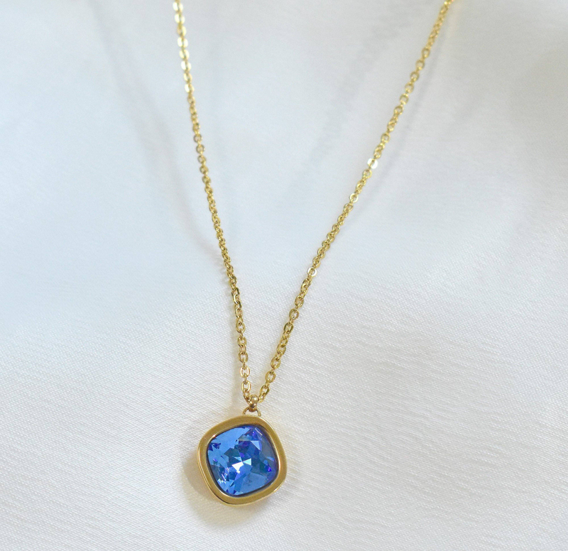 Gold pendant necklace with round blue gemstone in gold bezel, on chain