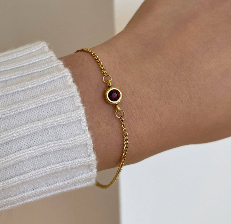Gold bracelet on wrist with red round birthstone bezel and linked chain
