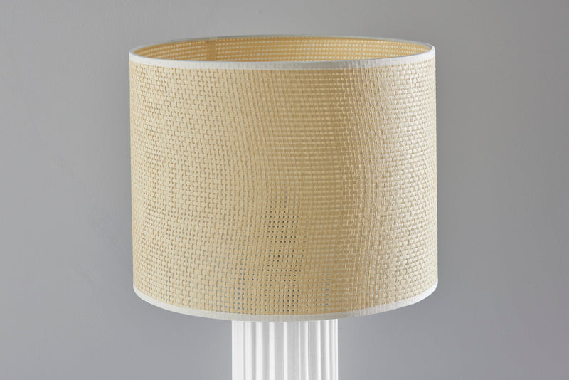 Table lamp showing beige woven drum shade over a white fluted base.