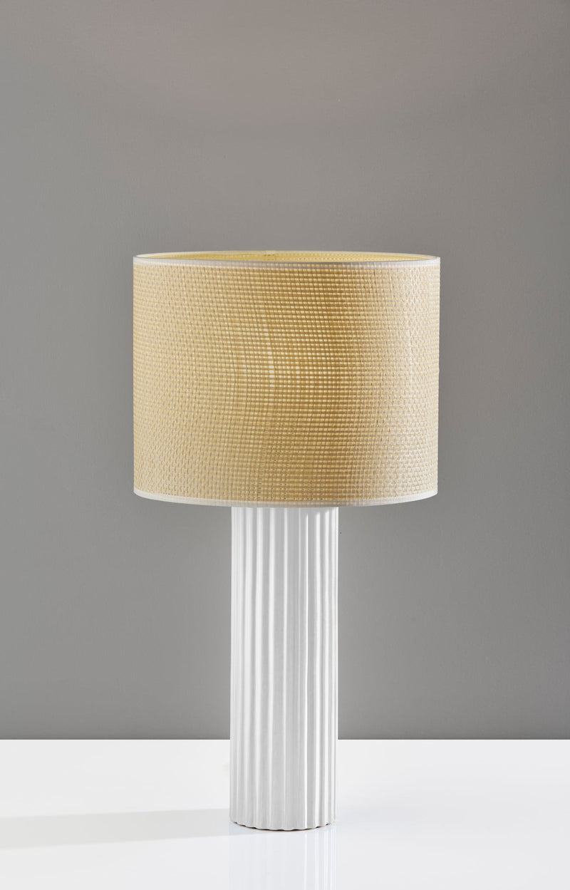 Table lamp standing with beige drum shade and white fluted base.