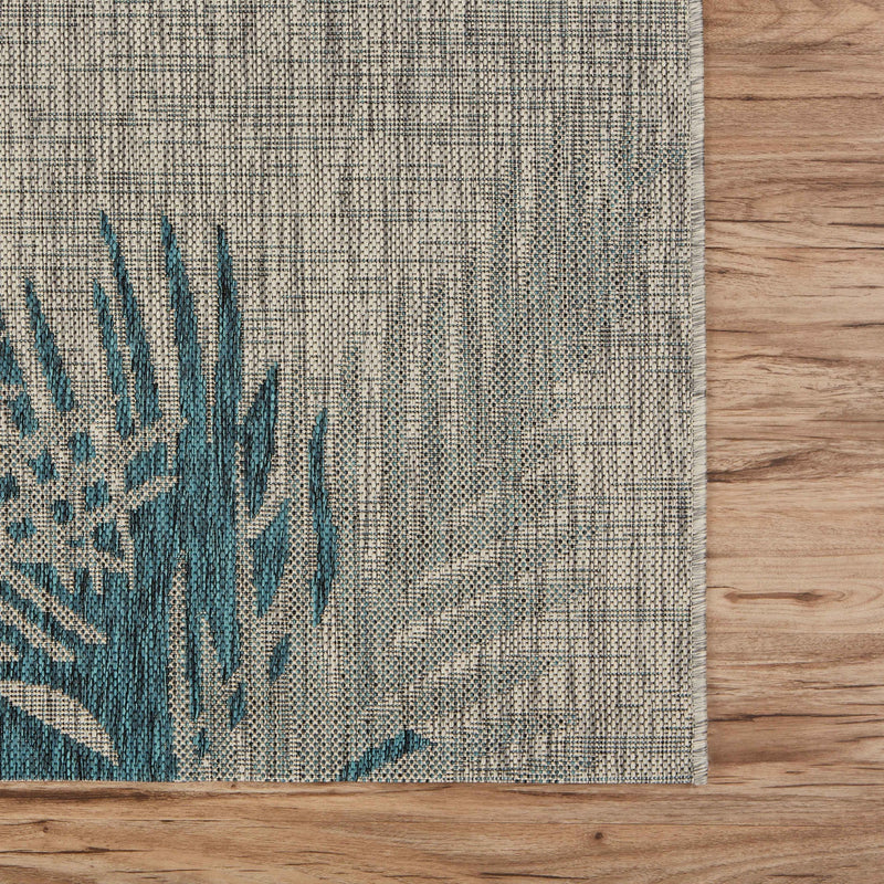Gray area rug corner with blue teal palm leaf motif on a tight woven grid texture.