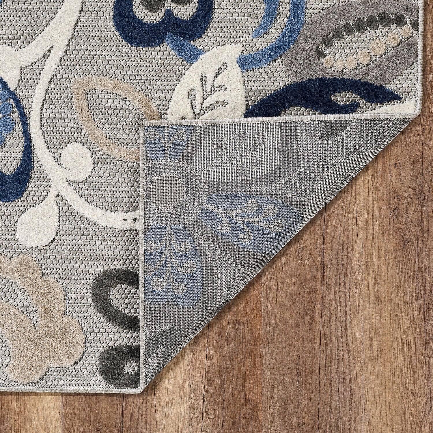 Indoor/outdoor area rug corner shown with gray and blue floral design, folded edge detail