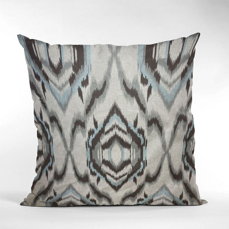 Studio view of an ikat patterned throw pillow in cream, dark gray, and light blue