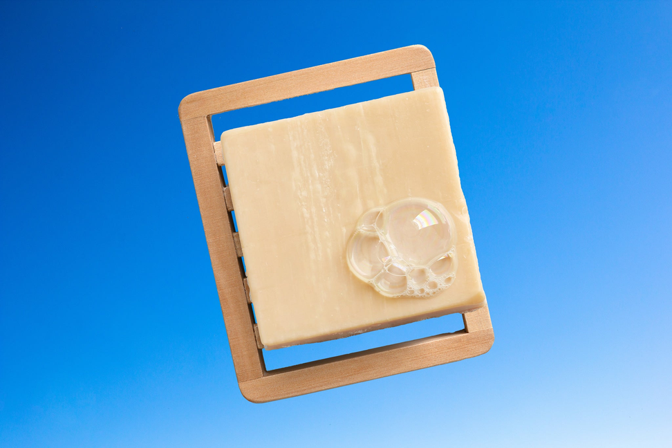 Goat milk body wash bar on wooden dish, light beige bar with embedded bubbles