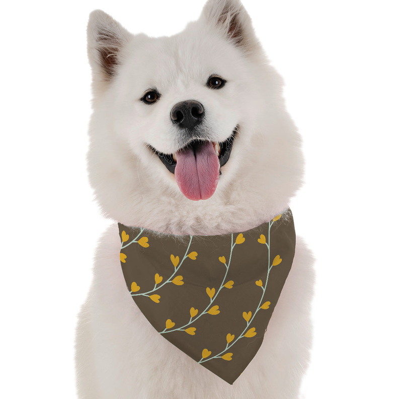 White dog wearing brown bandana with yellow leaf and heart pattern