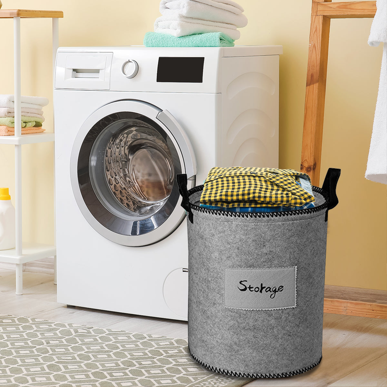 Gray felt laundry hamper with black handles and “Storage” label, holding folded yellow-and-white cloth.