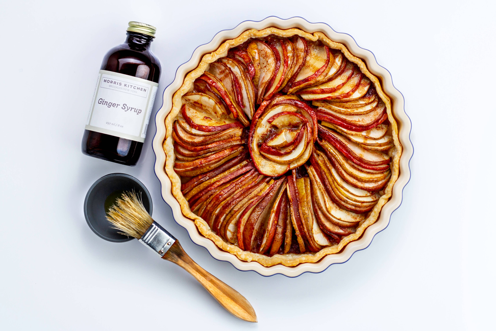 Ginger syrup bottle with gold cap near baked tart with sliced fruit glaze