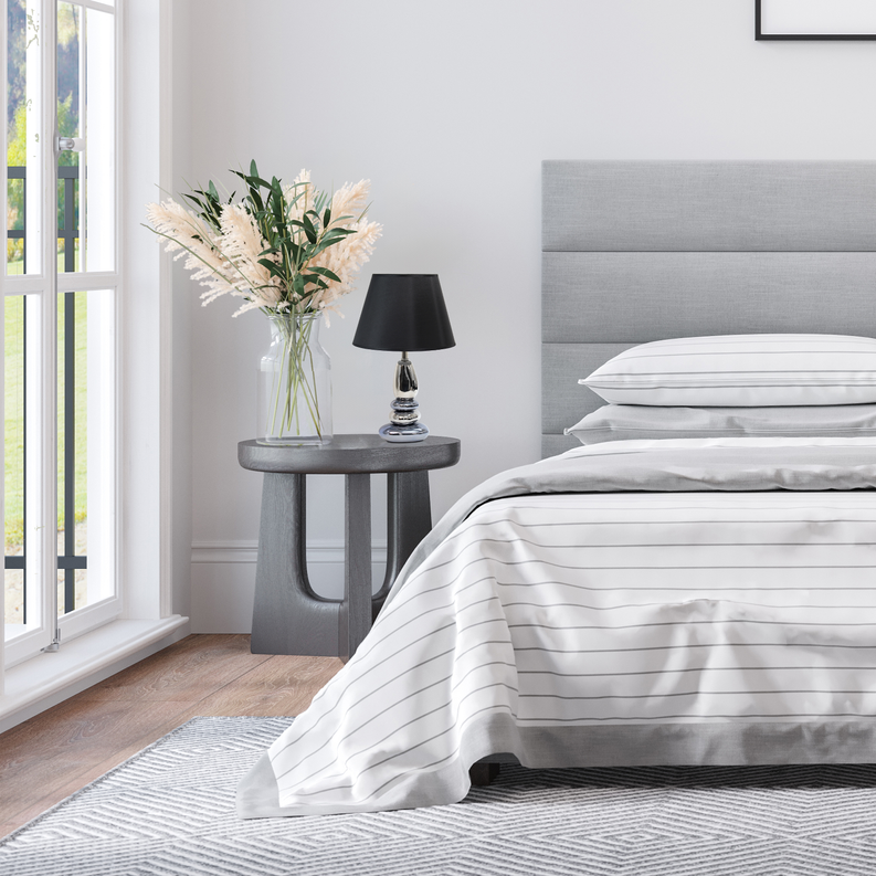 Black-shade chrome table lamp on round gray side table near bed