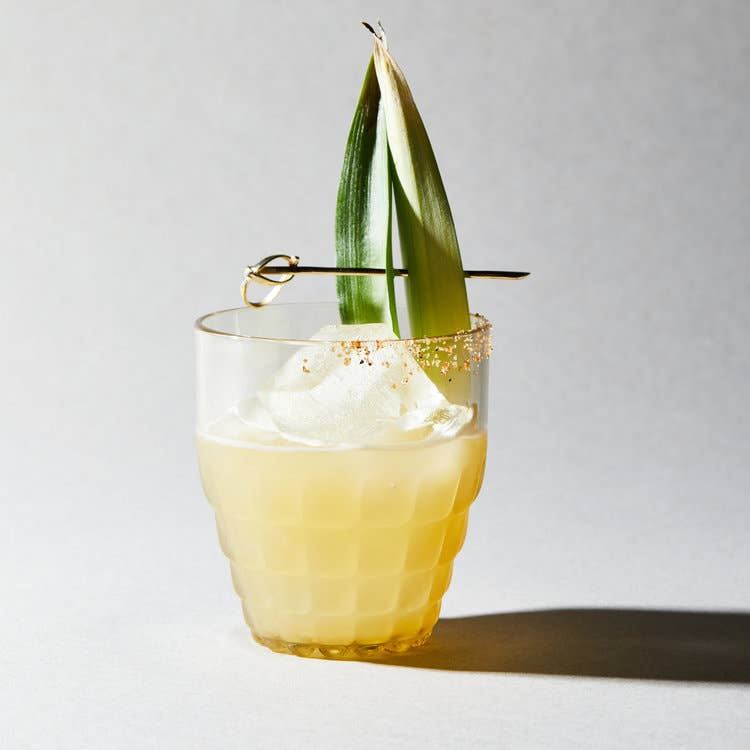 Pineapple-lime mixer cocktail in clear glass with lime peel garnish and ice