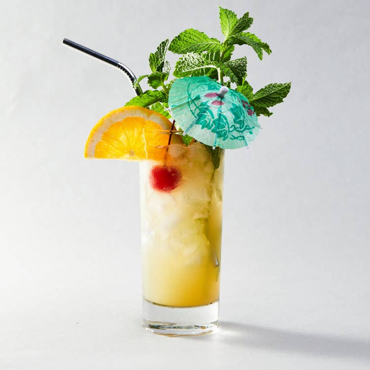 Pineapple-lime mixer cocktail in tall glass with mint, straw, orange slice, cherry