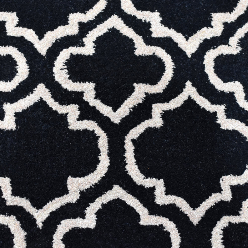 Black wool runner rug close-up with ivory quatrefoil trellis geometric pattern.