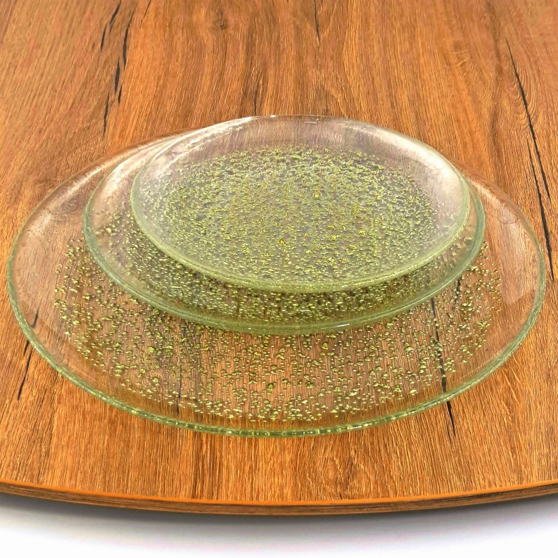 Stacked green-gold speckled glass dinner plates on wooden board, top plate visible.