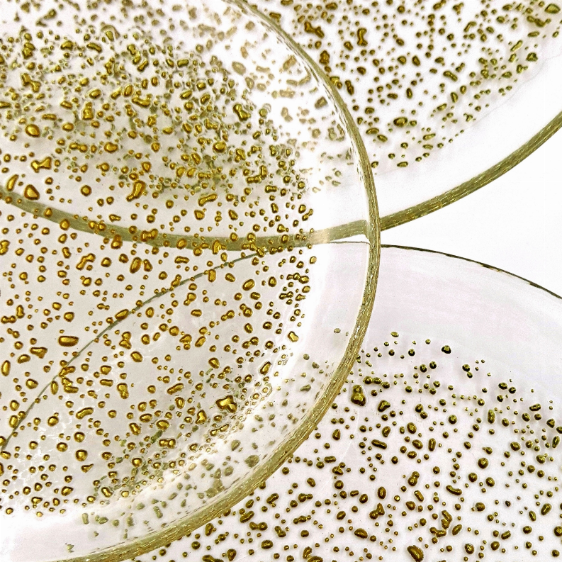 Close-up of clear glass dinner plates with gold speckled texture and curved rim.