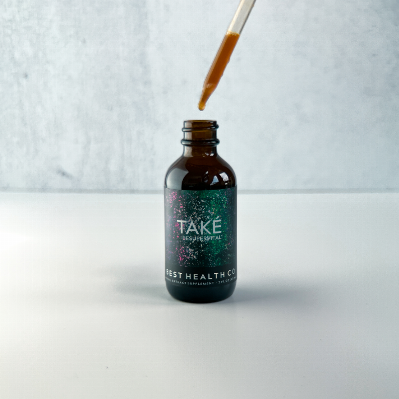 Amber glass dropper bottle with black cap, amber liquid drop mid-dispense.