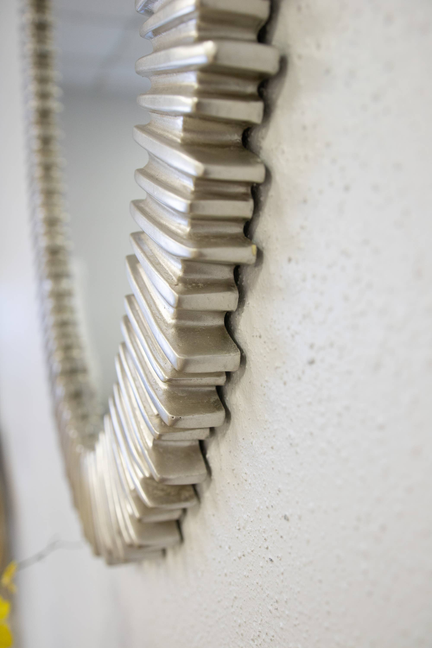 Close-up of brushed silver ribbed frame detail on an oval wall mirror.