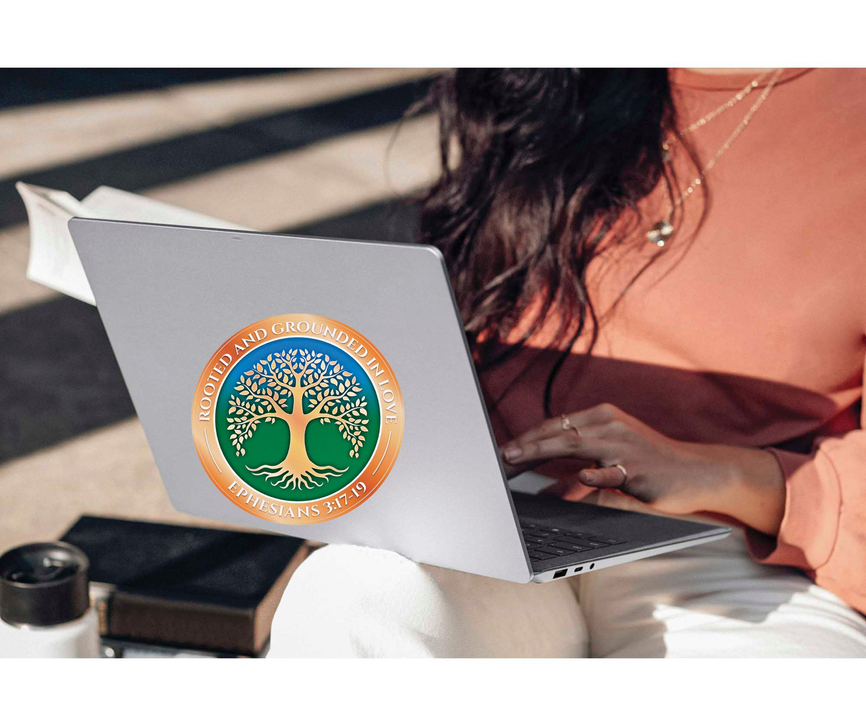 Rooted tree faith sticker on gray laptop lid, orange and green circular emblem