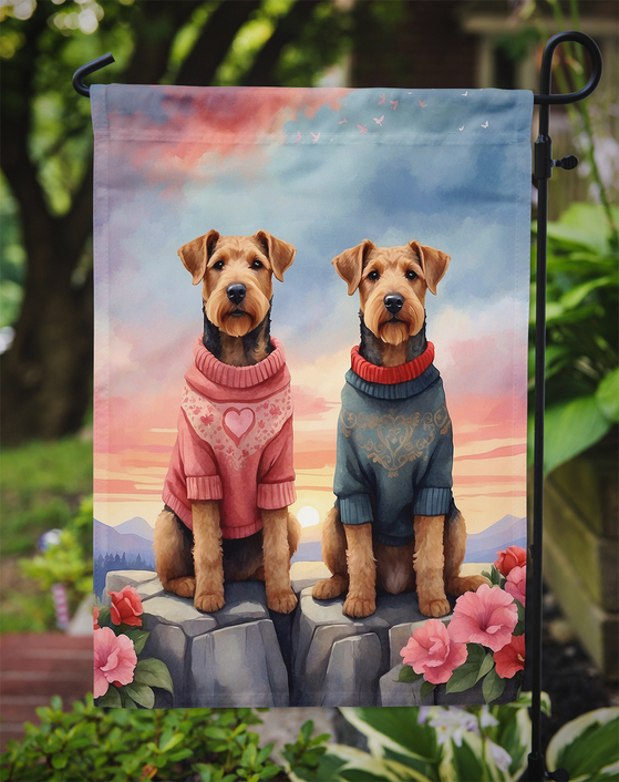 Two Airedale Terriers garden flag sitting on rocks under sunset sky with pink flowers