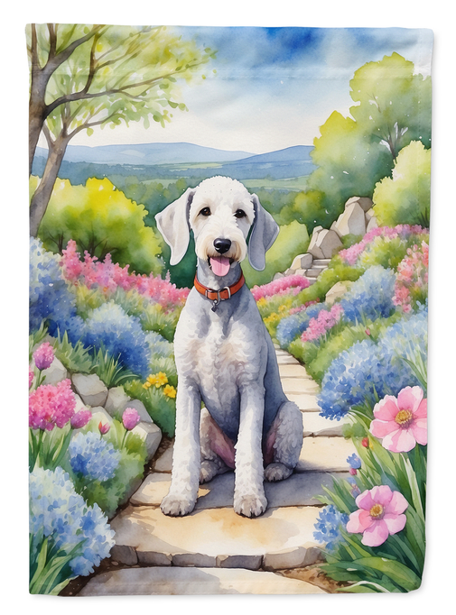 Garden flag close-up with Bedlington terrier on a stone path in colorful flowers