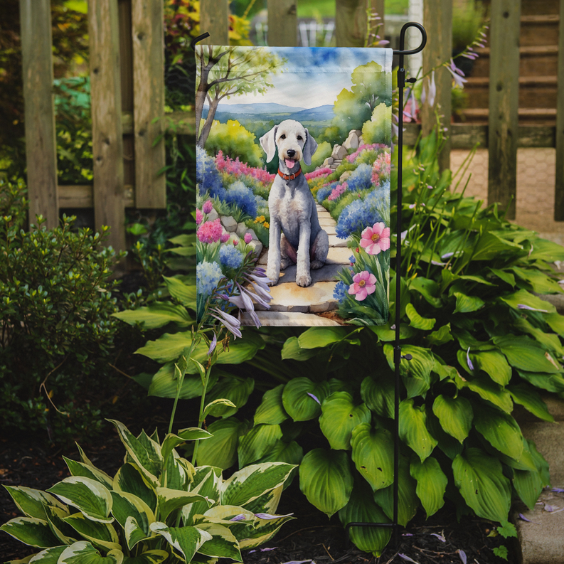 Garden flag hanging outdoors on a metal stand with a Bedlington terrier floral design