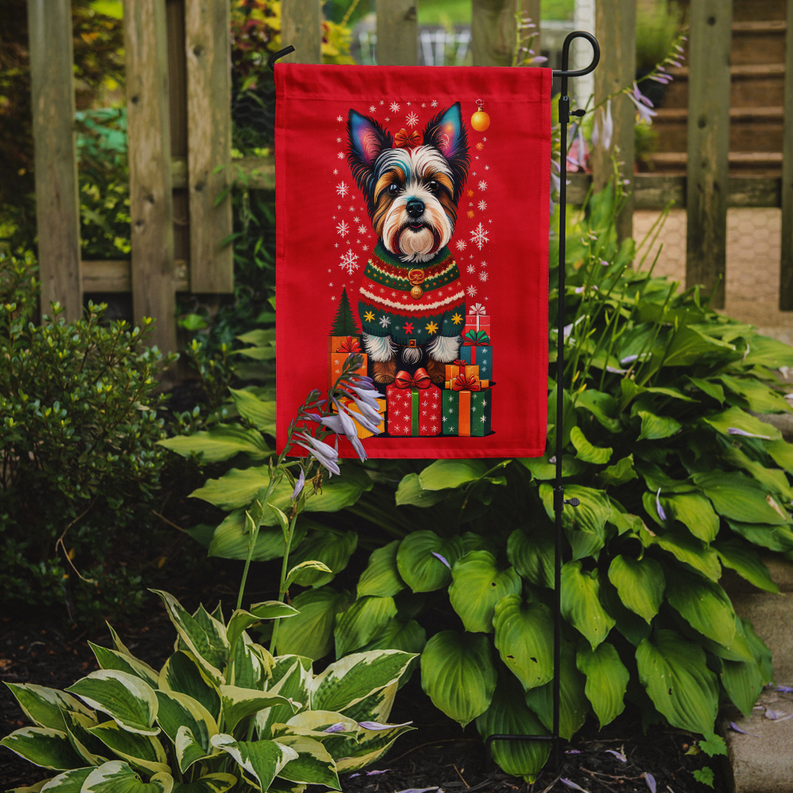 Red holiday garden flag on stake, terrier in sweater surrounded by Christmas gifts
