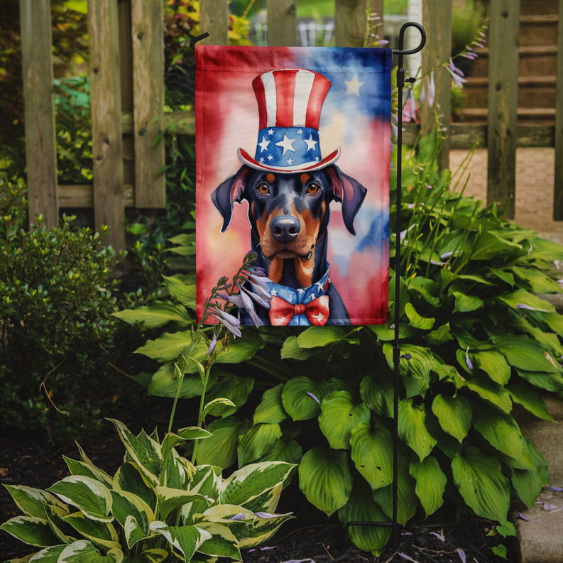 Patriotic Doberman garden flag on stake in a garden bed with leafy green plants