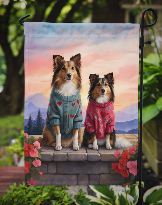 Garden flag with two shelties in heart sweaters standing on stone steps with flowers