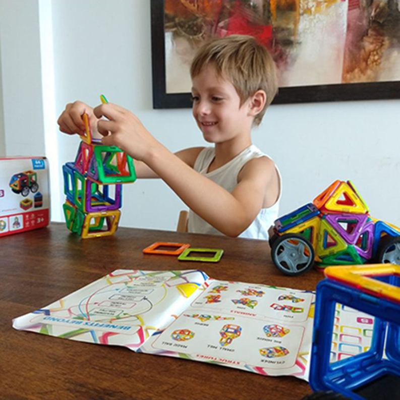 Boy holding a multicolor magnetic building block while wheeled blocks sit nearby