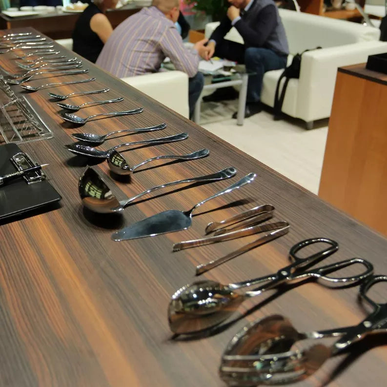 Stainless steel knife set lineup on a wooden display with polished handles and blades.