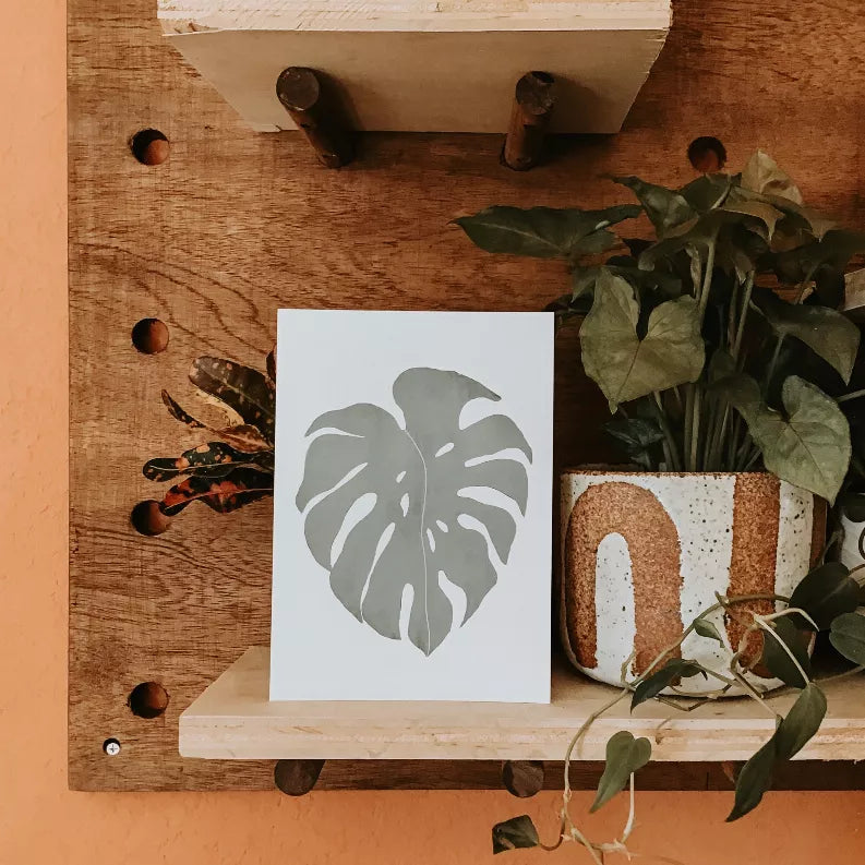 Monstera leaf art print on white paper with centered gray leaf graphic
