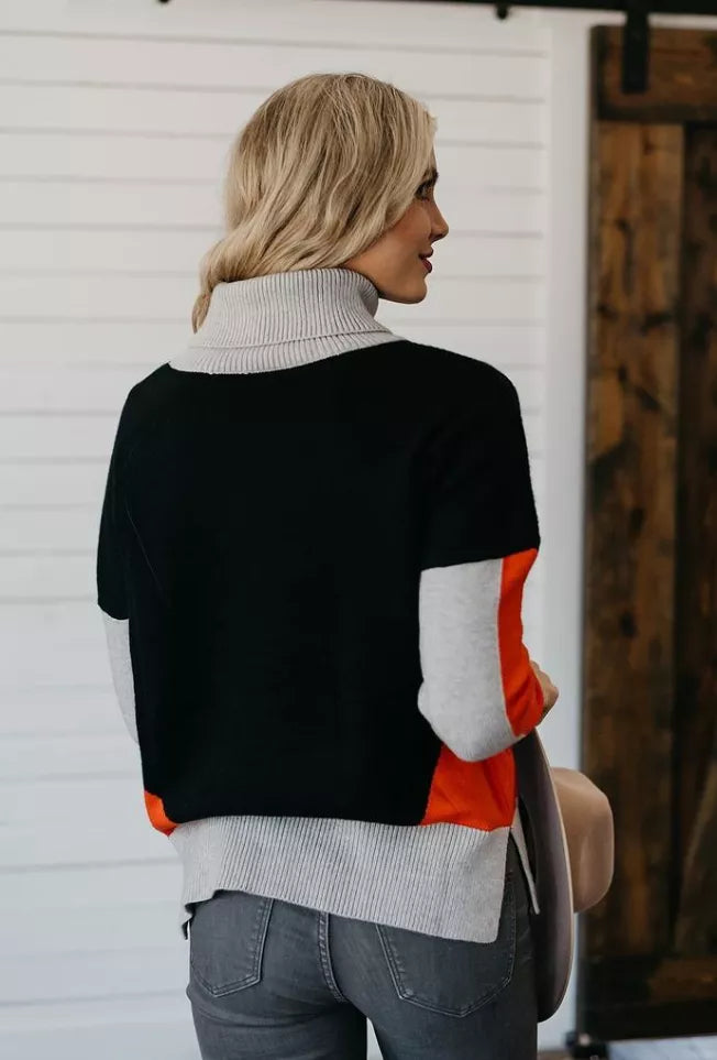 Back view: black color-block turtleneck sweater with orange side panel and light-gray sleeves