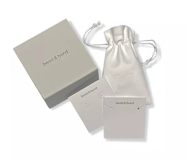 Gold hoop earrings in a drawstring pouch with brand card