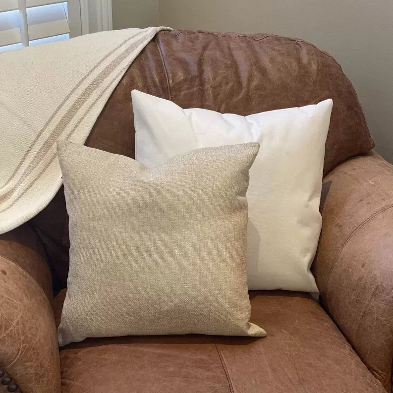 White pillow cover with stitched border, shown on a sofa with two throw pillows