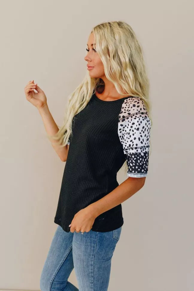 Black short-sleeve top with white spotted sleeves, front side view