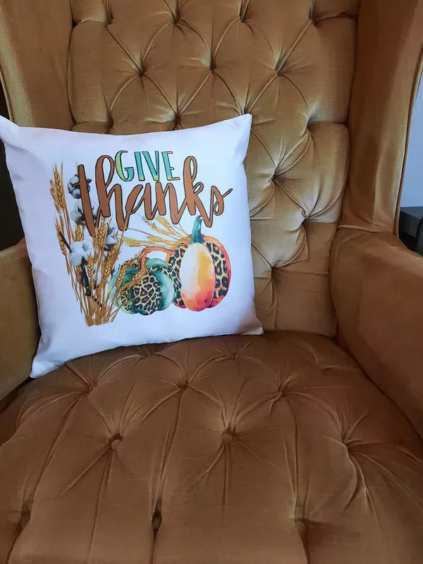White throw pillow reading 'Give thanks' with wheat, pumpkins, and gourds