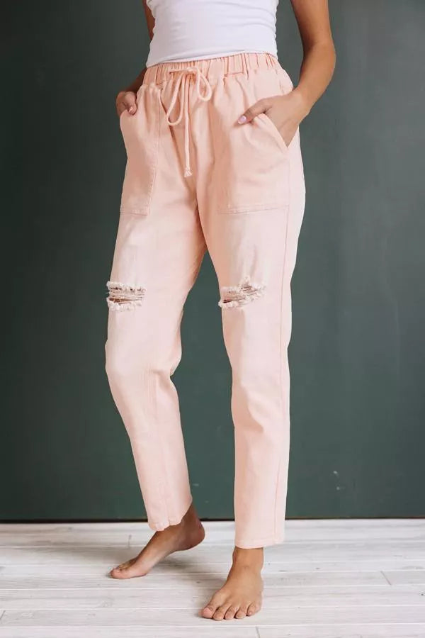 Pink denim joggers with drawstring, elastic waistband, frayed knee rips and ankle cuffs