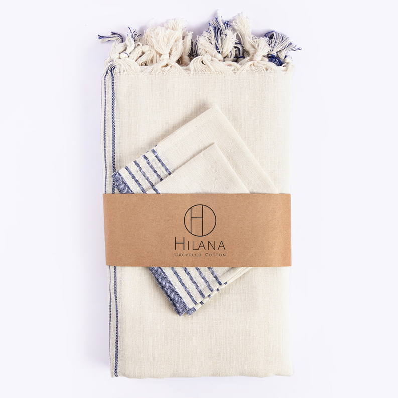 Packaged tablecloth set in cream fabric with blue striped edges and a kraft band
