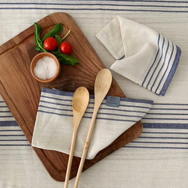 Cream-striped tablecloth napkins with blue bands, with wooden utensils on a board