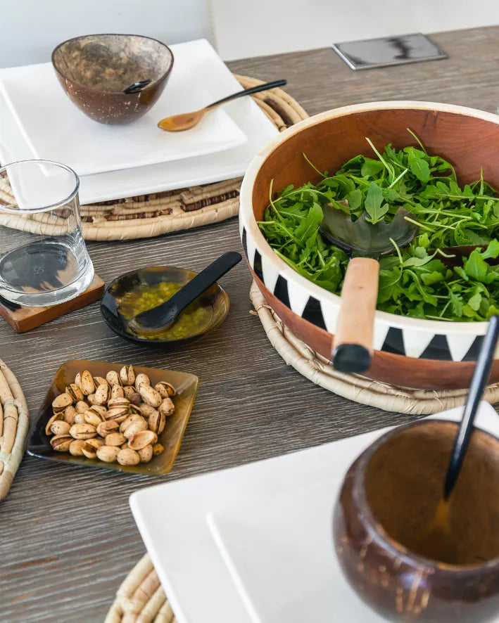 Round horn serving dish with black-and-white geometric rim, filled with greens