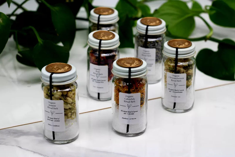 Assorted bath salt jars with gold lids, clear glass, and front labels grouped together.